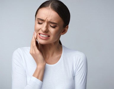 Woman with toothache standing against gray background